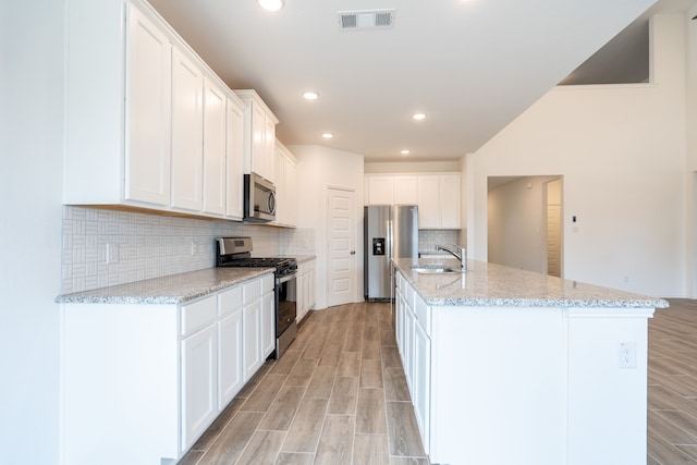 kitchen with light stone countertops, white cabinetry, appliances with stainless steel finishes, and a kitchen island with sink