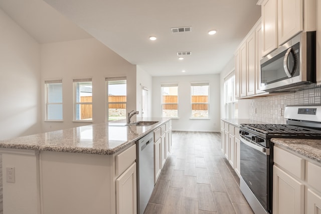 kitchen featuring sink, appliances with stainless steel finishes, a kitchen island with sink, tasteful backsplash, and white cabinets