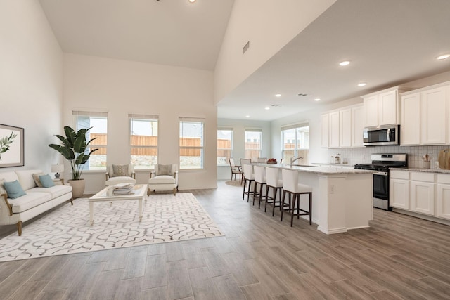 kitchen with a breakfast bar area, appliances with stainless steel finishes, white cabinets, a center island with sink, and light wood-type flooring