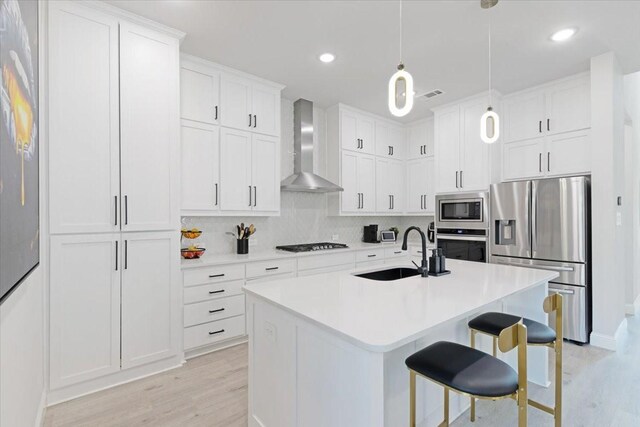 kitchen with sink, wall chimney exhaust hood, decorative light fixtures, white cabinetry, and stainless steel appliances