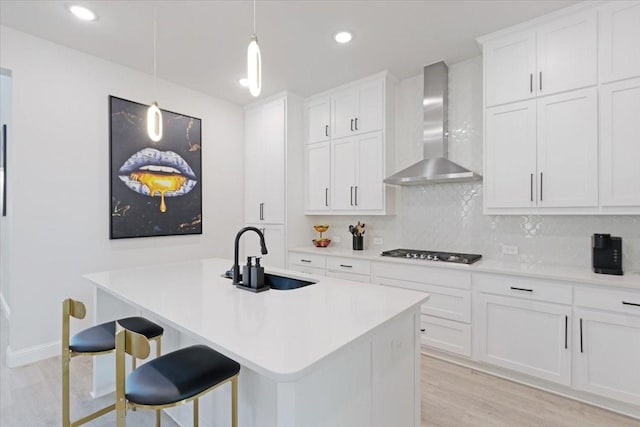 kitchen featuring tasteful backsplash, wall chimney exhaust hood, a breakfast bar, stainless steel gas cooktop, and white cabinets