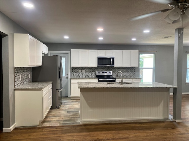 kitchen featuring appliances with stainless steel finishes, dark hardwood / wood-style floors, white cabinets, a kitchen island with sink, and light stone countertops