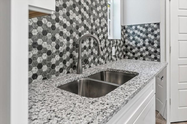 kitchen with backsplash, light stone counters, white cabinetry, and sink