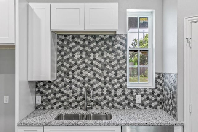 kitchen with dishwasher, white cabinets, sink, light stone countertops, and tasteful backsplash