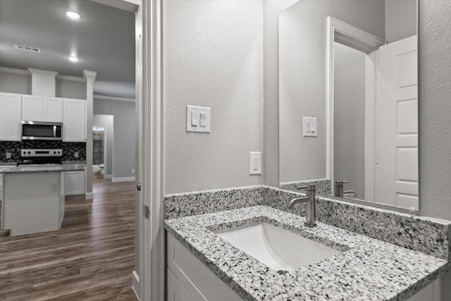 bathroom with hardwood / wood-style flooring, vanity, ornamental molding, and tasteful backsplash