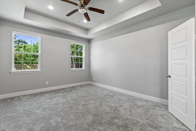 empty room with carpet flooring, a raised ceiling, and ceiling fan