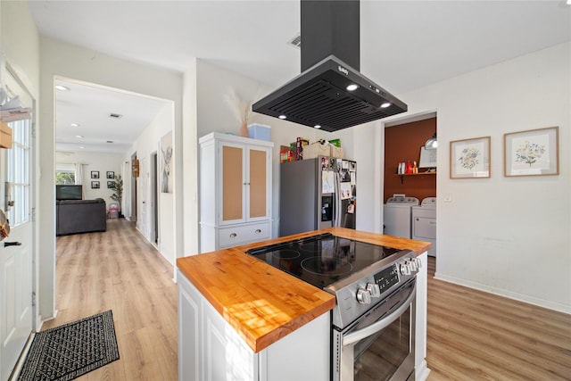 kitchen featuring butcher block countertops, island exhaust hood, washer and clothes dryer, white cabinets, and appliances with stainless steel finishes