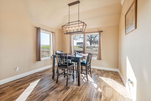 dining area with lofted ceiling, wood-type flooring, and an inviting chandelier