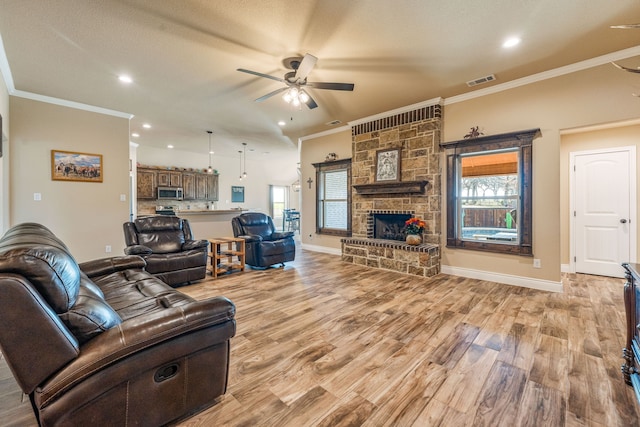 living room with ceiling fan, crown molding, light wood-type flooring, and a fireplace