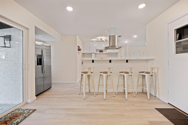 kitchen with white cabinets, a kitchen breakfast bar, kitchen peninsula, light hardwood / wood-style flooring, and stainless steel fridge with ice dispenser