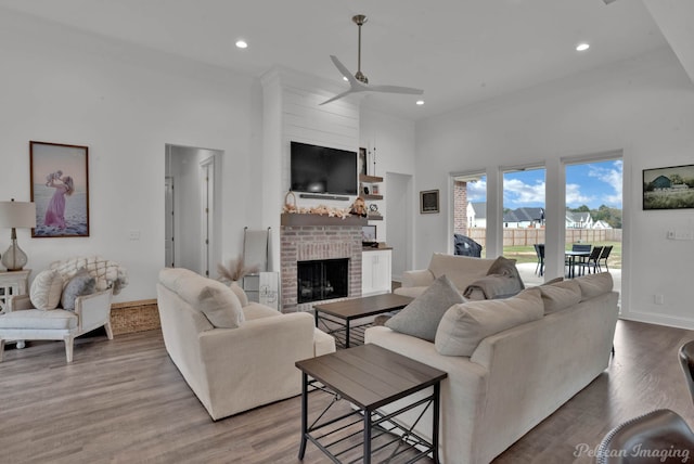 living room with ceiling fan, a high ceiling, a brick fireplace, and light wood-type flooring