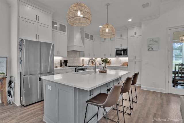 kitchen featuring wall chimney range hood, stainless steel fridge, a kitchen island with sink, hanging light fixtures, and white cabinets