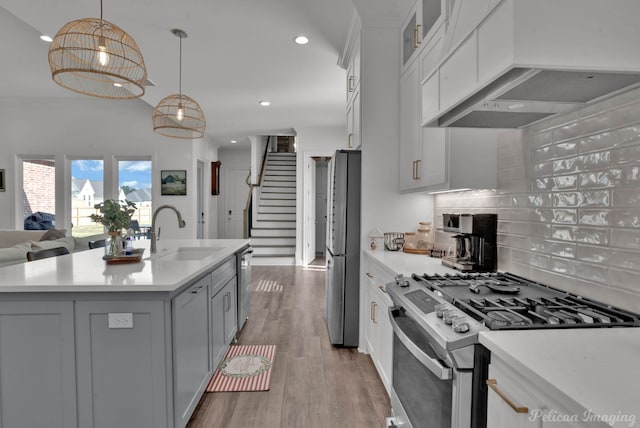 kitchen with sink, premium range hood, a kitchen island with sink, appliances with stainless steel finishes, and decorative light fixtures