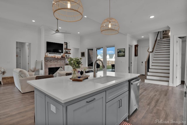 kitchen with sink, decorative light fixtures, a brick fireplace, stainless steel dishwasher, and a kitchen island with sink