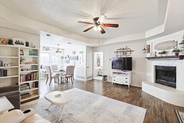 living room featuring a brick fireplace, ceiling fan, a textured ceiling, and a tray ceiling