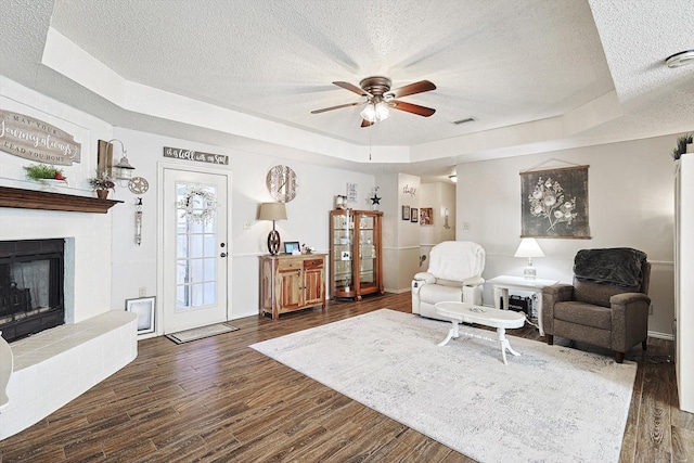 living room with a raised ceiling, a fireplace, ceiling fan, and dark hardwood / wood-style flooring