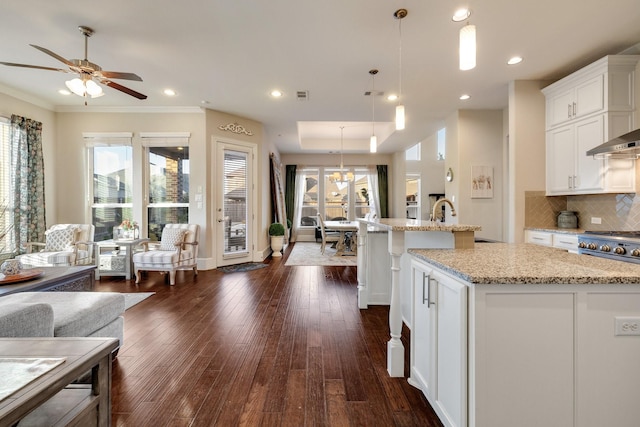 kitchen featuring hanging light fixtures, white cabinetry, a center island with sink, and light stone counters