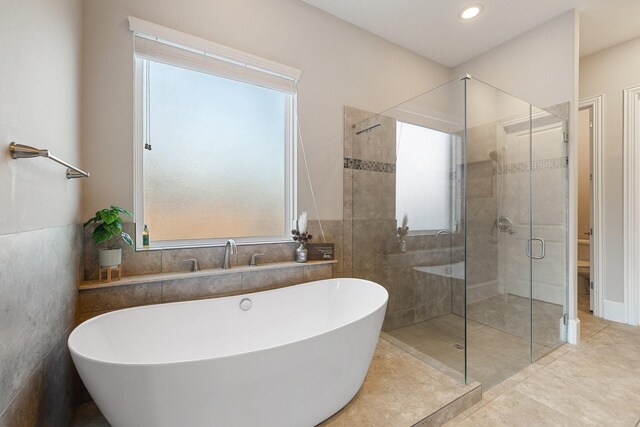 bathroom with a healthy amount of sunlight, independent shower and bath, and tile walls