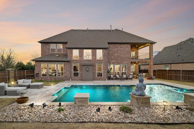 pool at dusk with outdoor lounge area and a patio