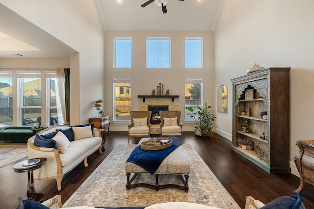 living room with a stone fireplace, a wealth of natural light, dark hardwood / wood-style flooring, ornamental molding, and ceiling fan