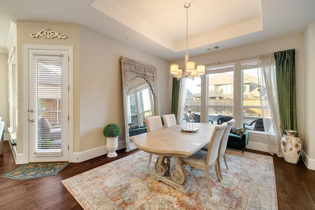 dining space with an inviting chandelier, dark hardwood / wood-style floors, and a raised ceiling