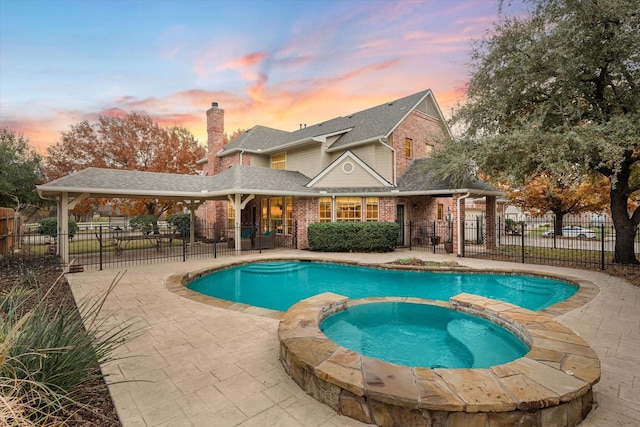 pool at dusk featuring a patio and an in ground hot tub