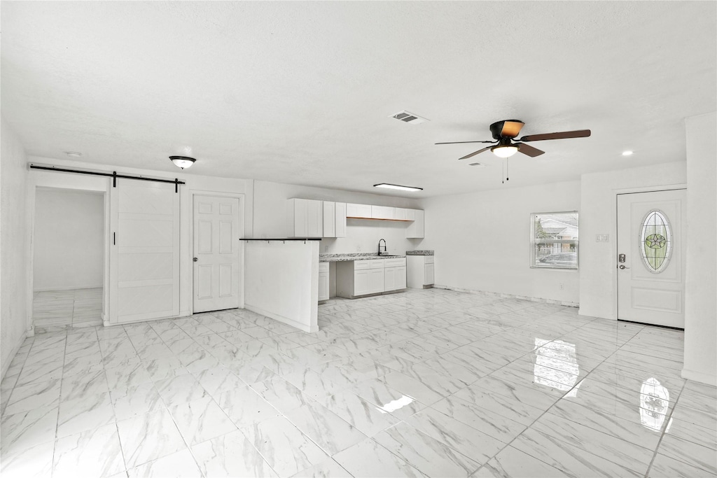 unfurnished living room with ceiling fan, a barn door, and sink