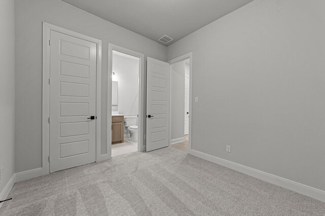 unfurnished bedroom with light colored carpet and connected bathroom