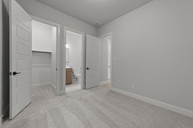 unfurnished bedroom featuring a spacious closet, light colored carpet, a closet, and ensuite bathroom