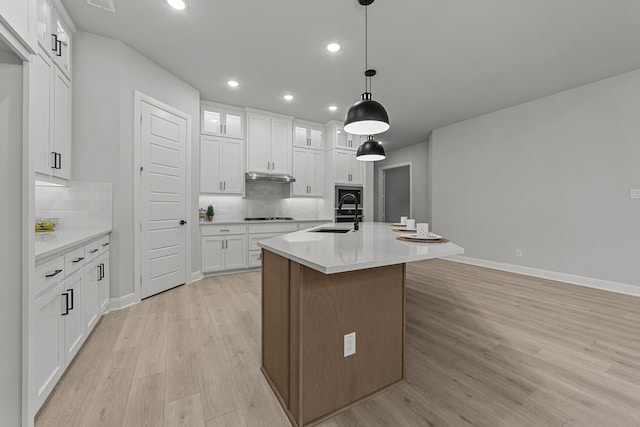 kitchen with decorative light fixtures, a kitchen island with sink, light hardwood / wood-style flooring, and white cabinets