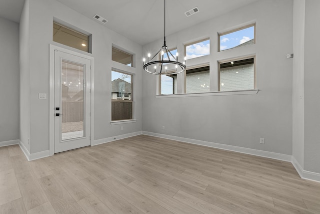 unfurnished dining area featuring an inviting chandelier, a wealth of natural light, and light wood-type flooring