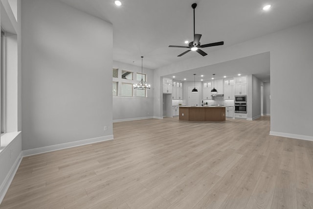 unfurnished living room featuring sink, ceiling fan with notable chandelier, and light hardwood / wood-style floors