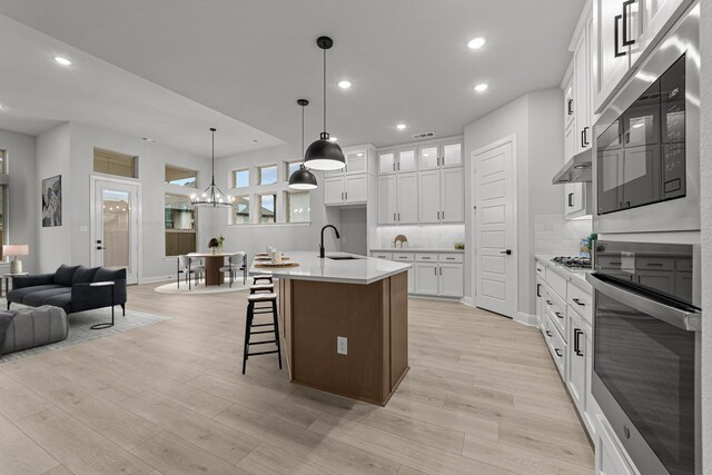 kitchen featuring sink, decorative light fixtures, light hardwood / wood-style flooring, an island with sink, and white cabinets