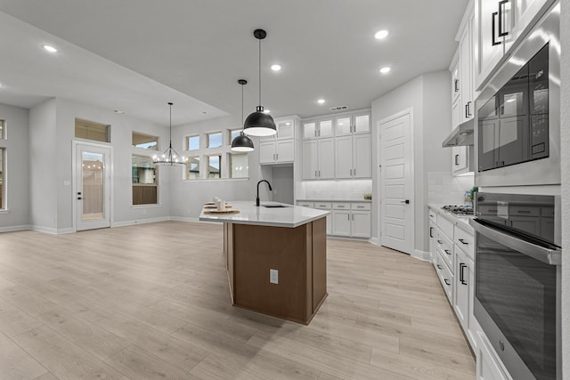 kitchen featuring pendant lighting, sink, white cabinets, light hardwood / wood-style floors, and a center island with sink