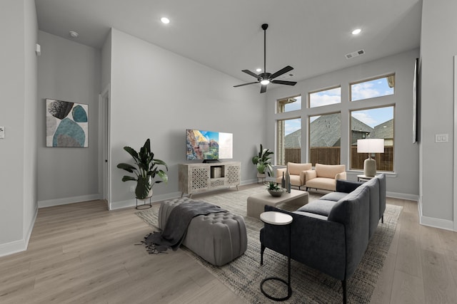 living room with ceiling fan, light hardwood / wood-style floors, and a high ceiling