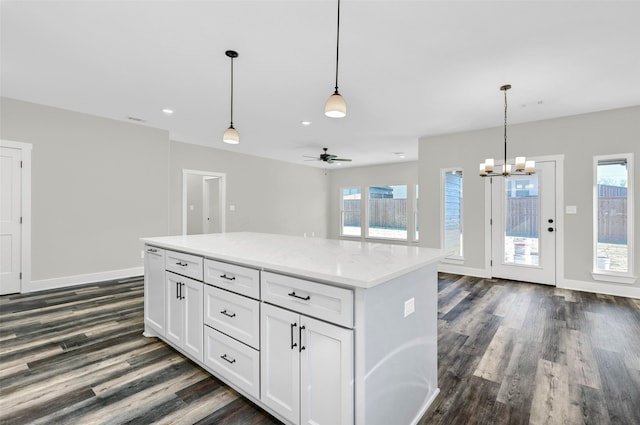 kitchen with decorative light fixtures, white cabinets, dark hardwood / wood-style flooring, a center island, and light stone counters