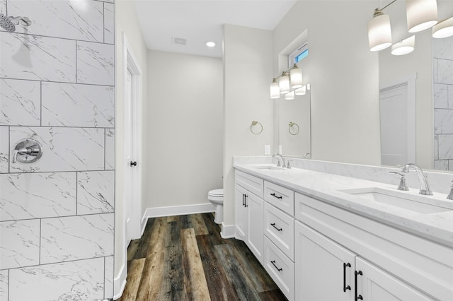 bathroom with hardwood / wood-style flooring, vanity, tiled shower, and toilet