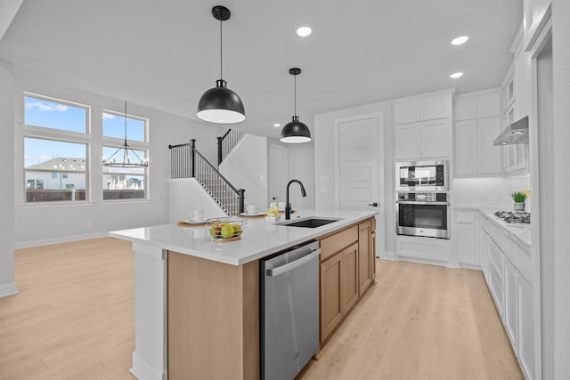 kitchen with a sink, light countertops, appliances with stainless steel finishes, light wood finished floors, and a center island with sink