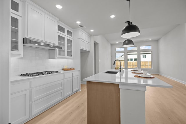 kitchen with light wood-style flooring, a sink, under cabinet range hood, stainless steel gas stovetop, and backsplash