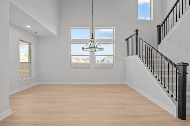 interior space with a high ceiling, an inviting chandelier, light wood-style flooring, and baseboards