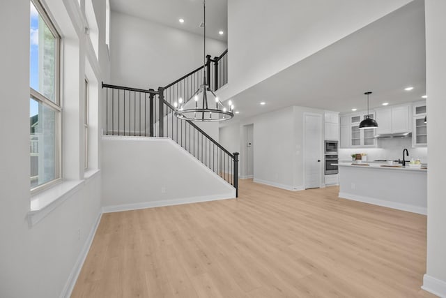 unfurnished living room featuring light wood-type flooring, a high ceiling, stairway, and baseboards