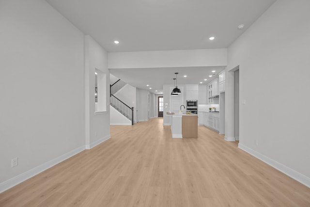 unfurnished living room featuring light wood finished floors, stairs, baseboards, and recessed lighting