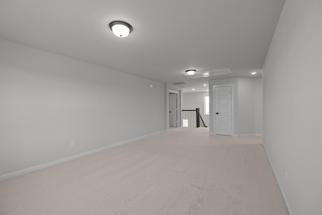 empty room with visible vents, baseboards, attic access, and light colored carpet