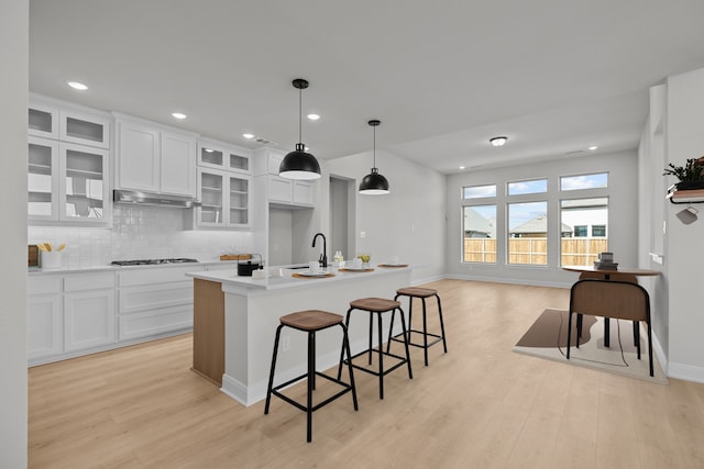 kitchen with light wood-style flooring, decorative backsplash, white cabinetry, a sink, and under cabinet range hood