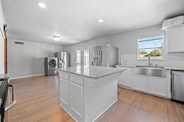 kitchen with sink, appliances with stainless steel finishes, a center island, white cabinets, and washer / clothes dryer