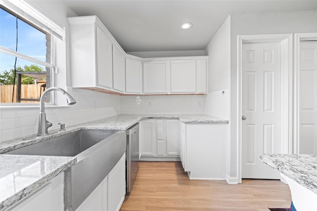 kitchen with sink, light hardwood / wood-style flooring, light stone counters, white cabinets, and stainless steel dishwasher