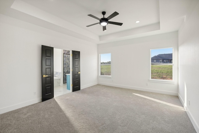 unfurnished bedroom with ensuite bathroom, a raised ceiling, and carpet floors