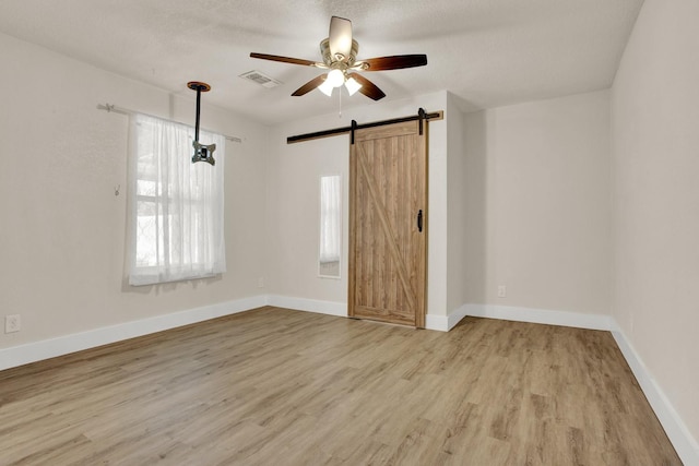 unfurnished room with a barn door, light hardwood / wood-style floors, a wealth of natural light, and ceiling fan