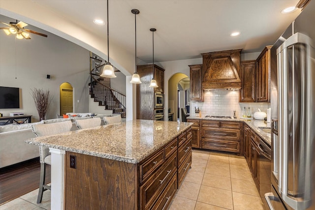 kitchen featuring a breakfast bar, premium range hood, appliances with stainless steel finishes, hanging light fixtures, and a kitchen island