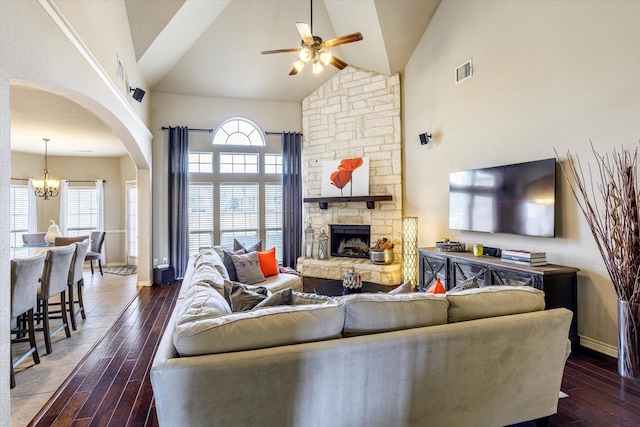 living room with a fireplace, ceiling fan with notable chandelier, dark wood-type flooring, and high vaulted ceiling